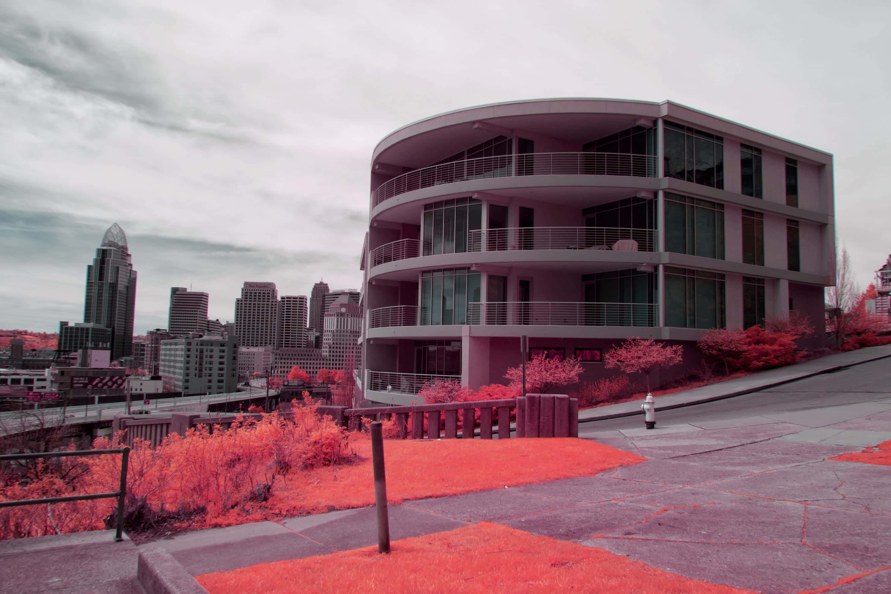 The downtown Cincinnati skyline seen past a curved apartment building from a hillside above the city, photographed in near-infrared light.