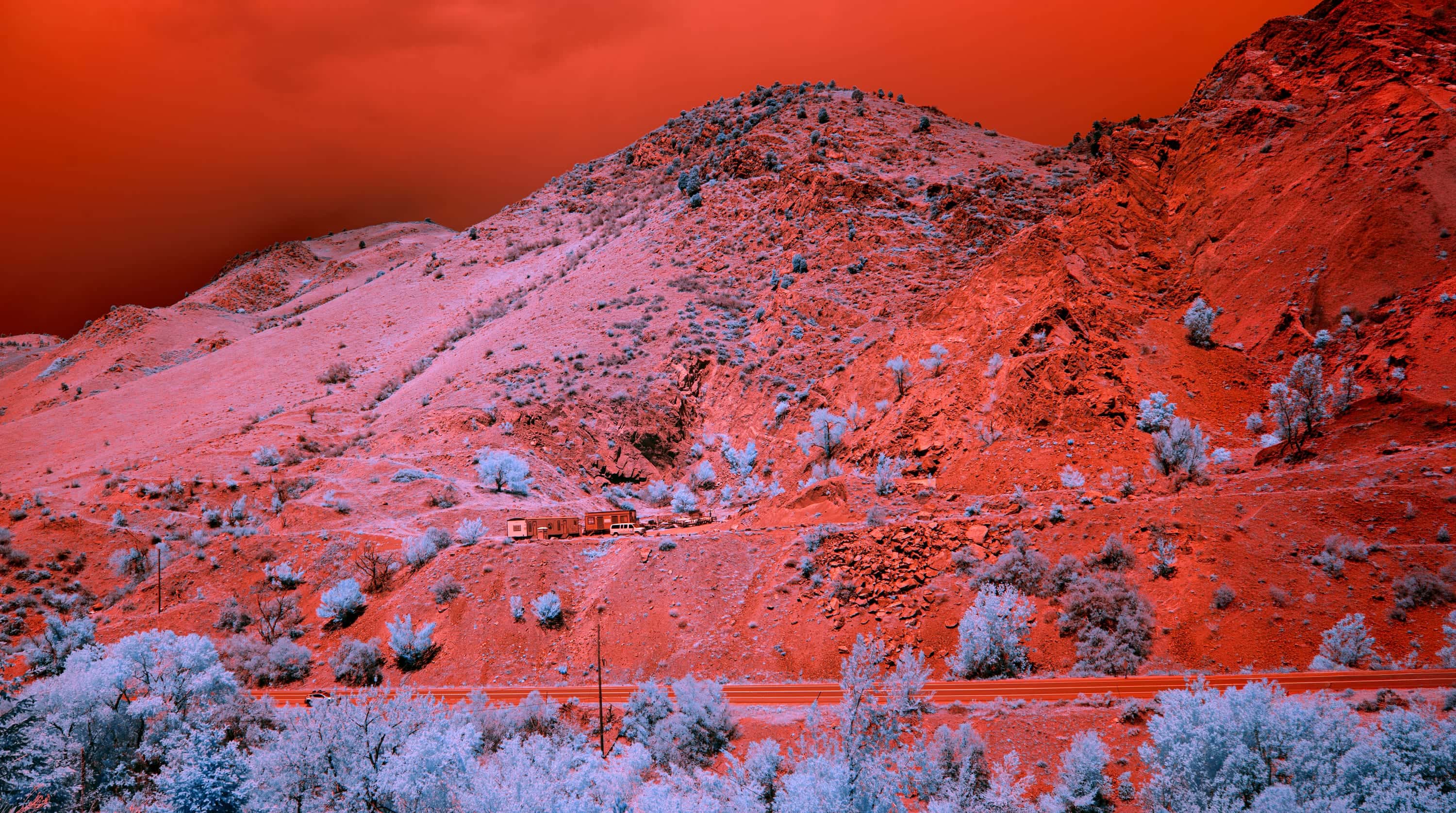 A construction trailer and a van parked on a bench cut into a dry hillside above a two-lane highway near Denver, photographed in near-infrared light.