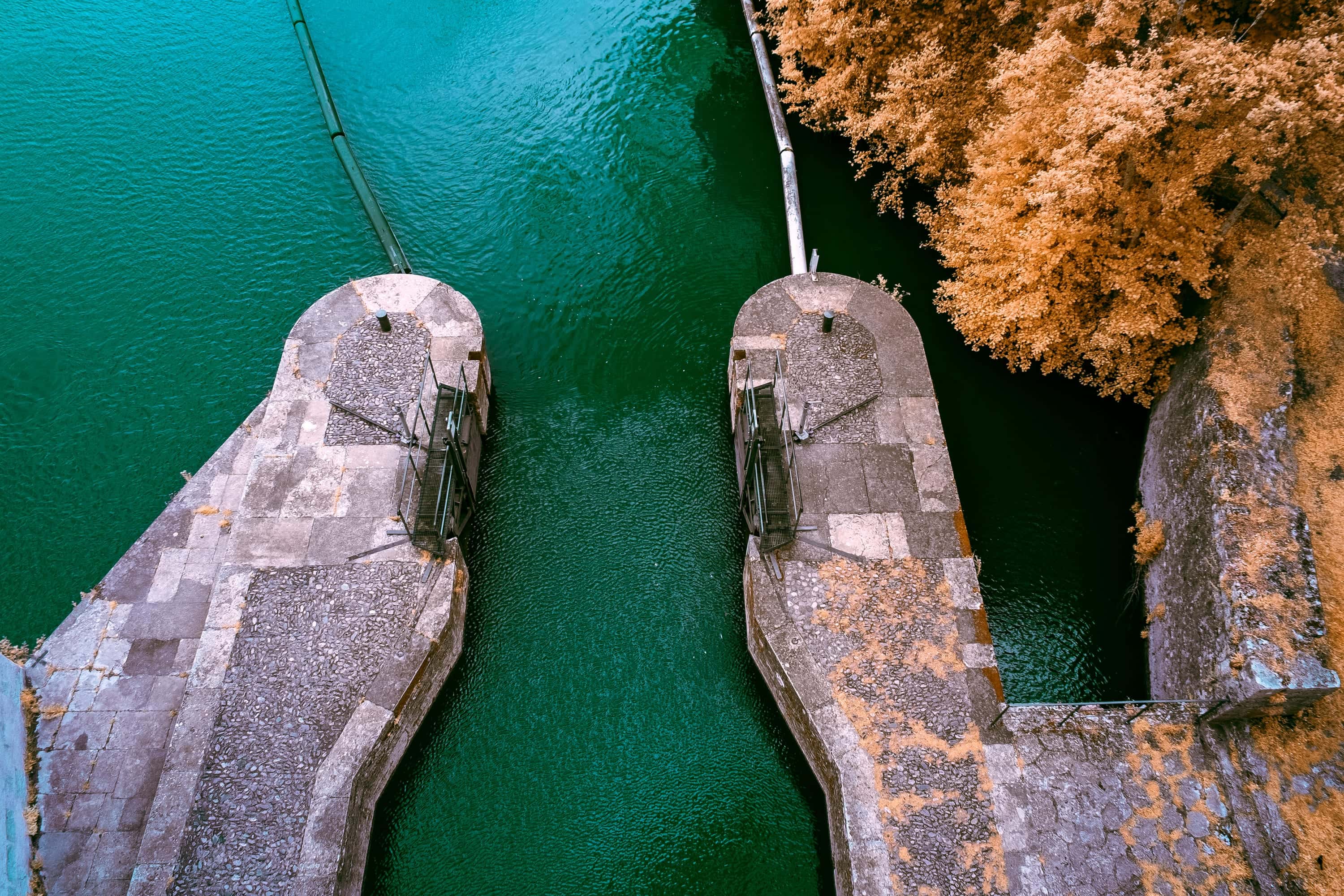 Two stone piers in a river channel with metal frames on top of each, seen from directly above, photographed in near-infrared light.