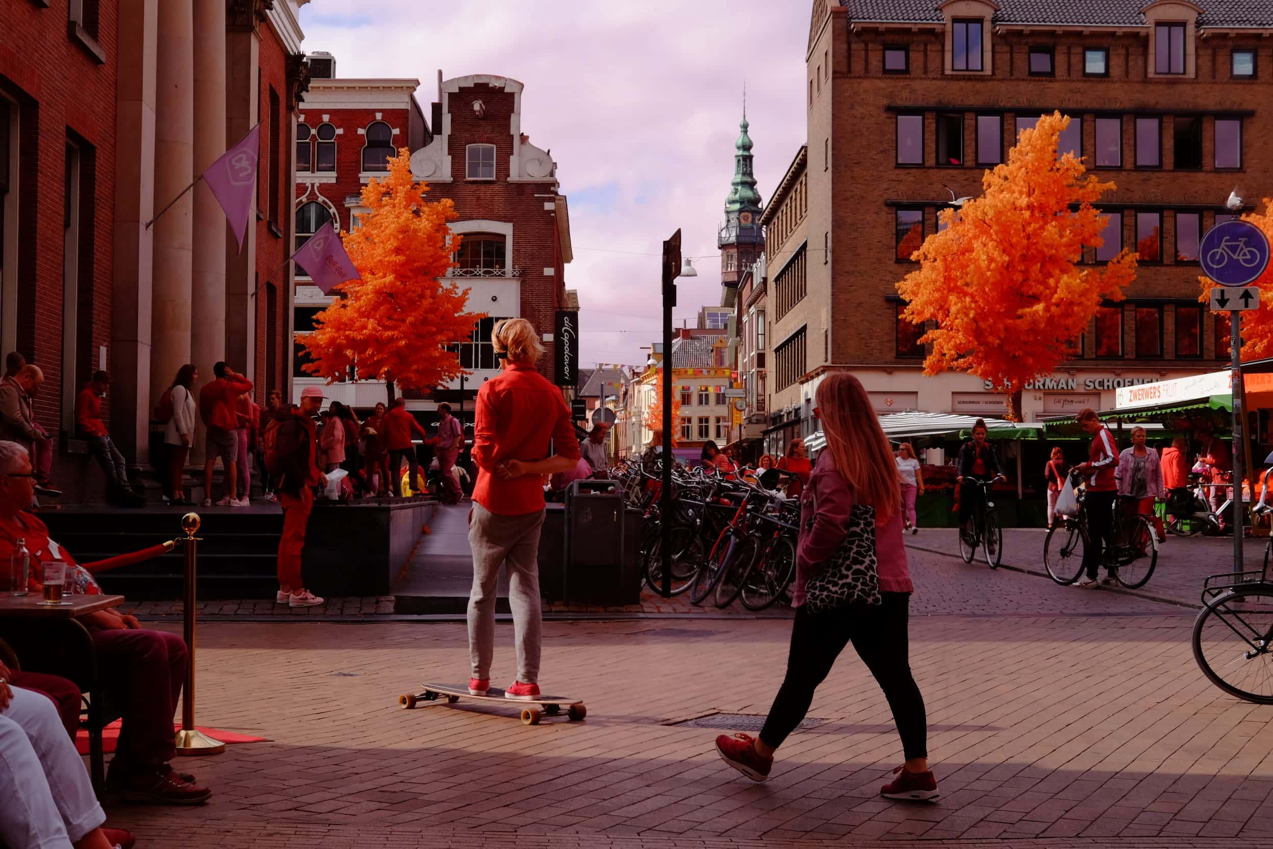 A Dutch market square — a skateboarder, cyclists and awnings under trees gone bright orange